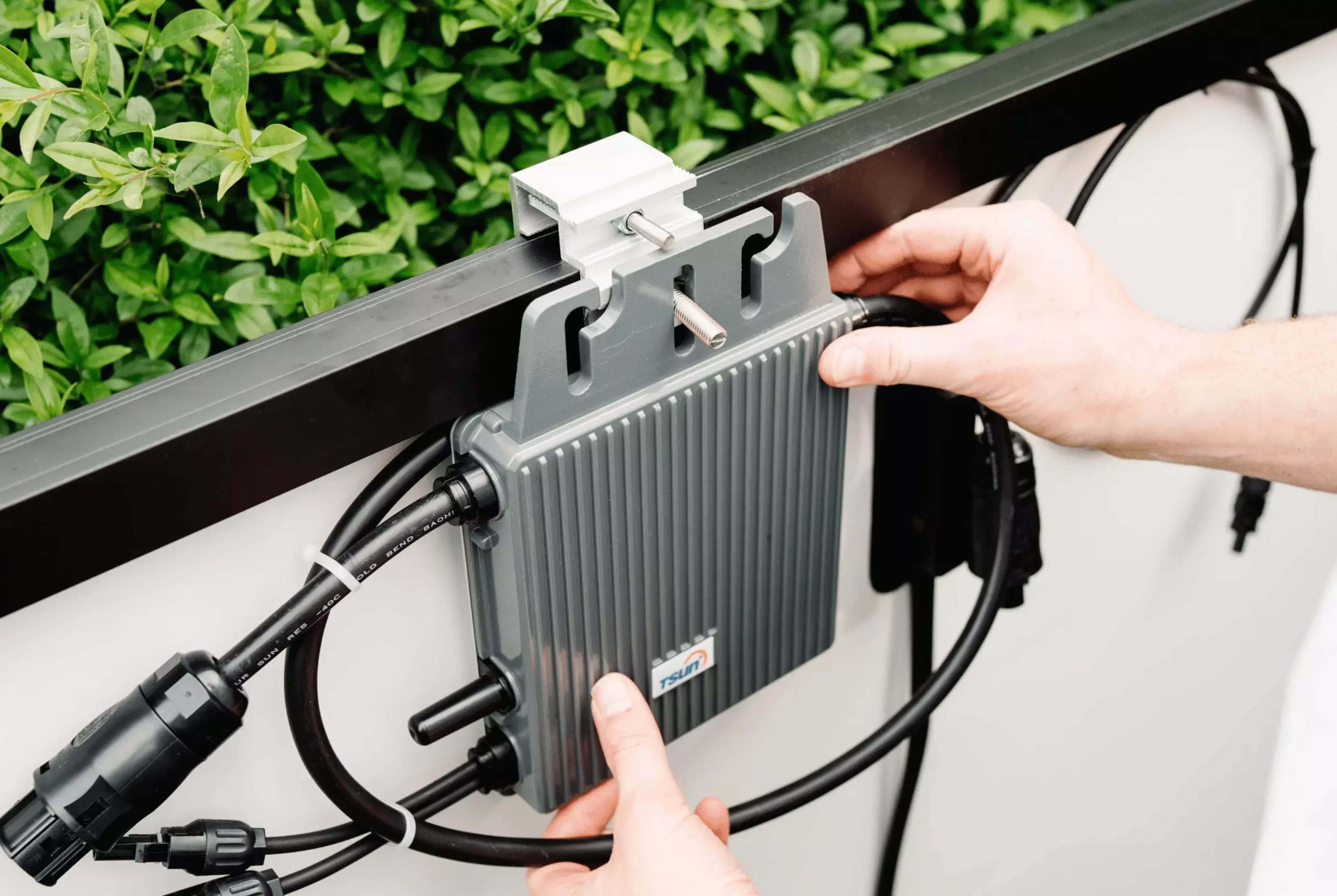 Mann befestigt Wechselrichter an Balkongeländer.