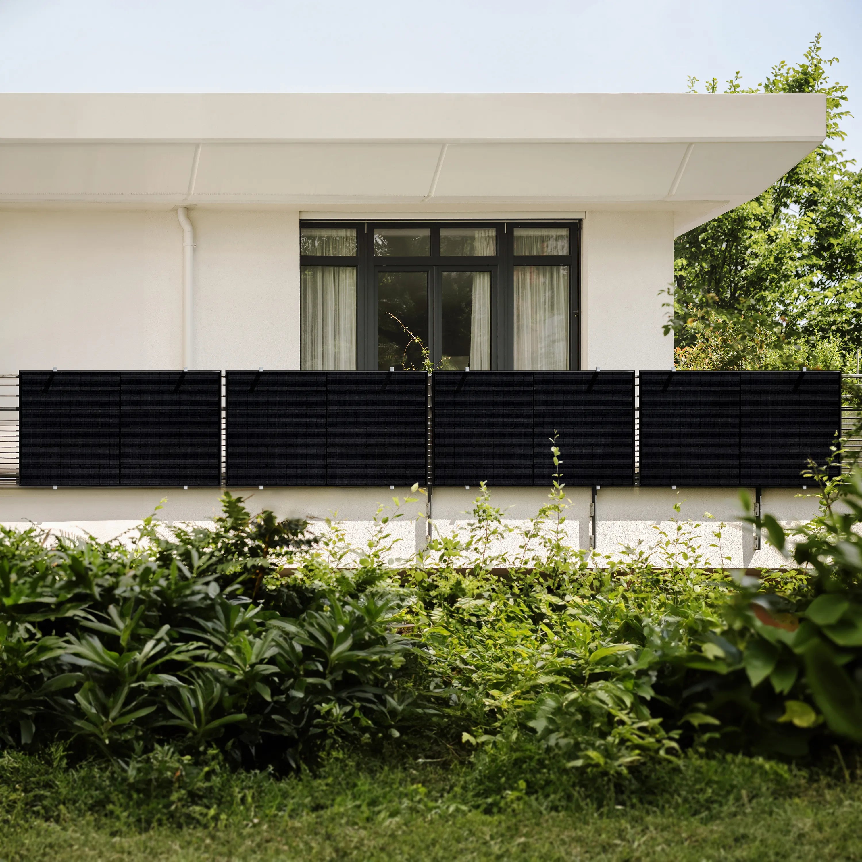 4 schwarze Solarmodule befestigt an einem modernen Balkon mit weißer Fassade