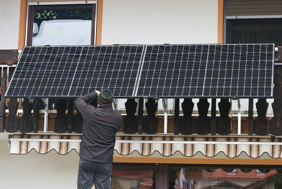 Mann montiert ein Balkonkraftwerk mit kleinen Solarpanels am Balkongeländer.