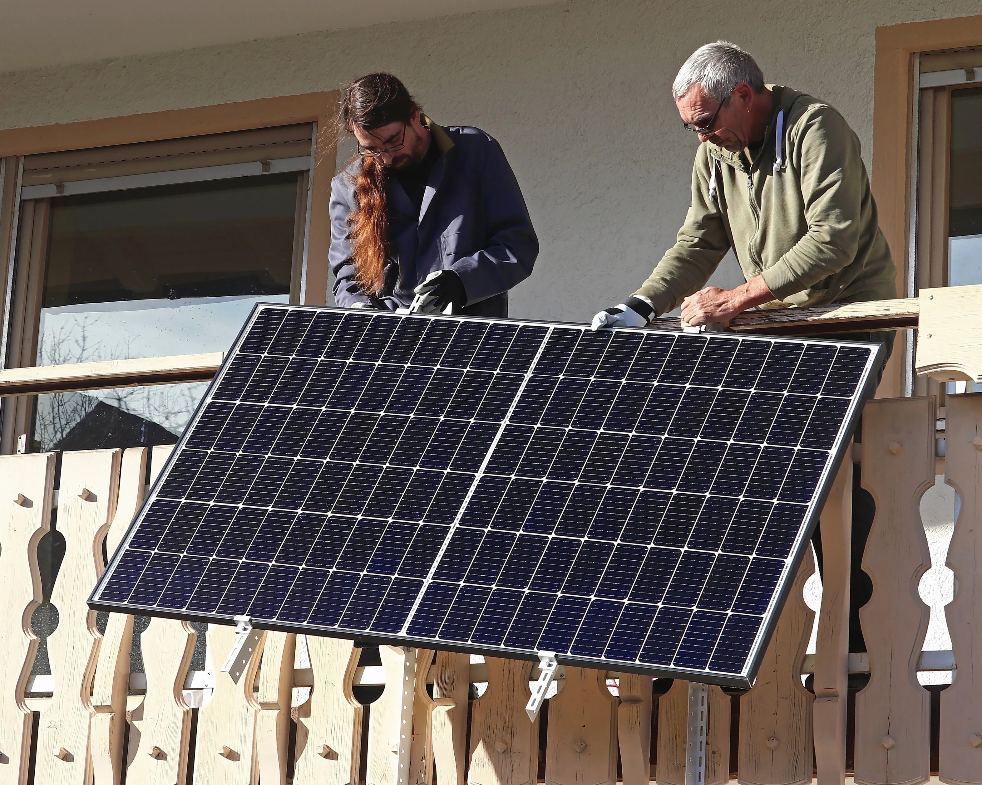 Solarmodul wird von zwei Männern auf dem Balkon montiert