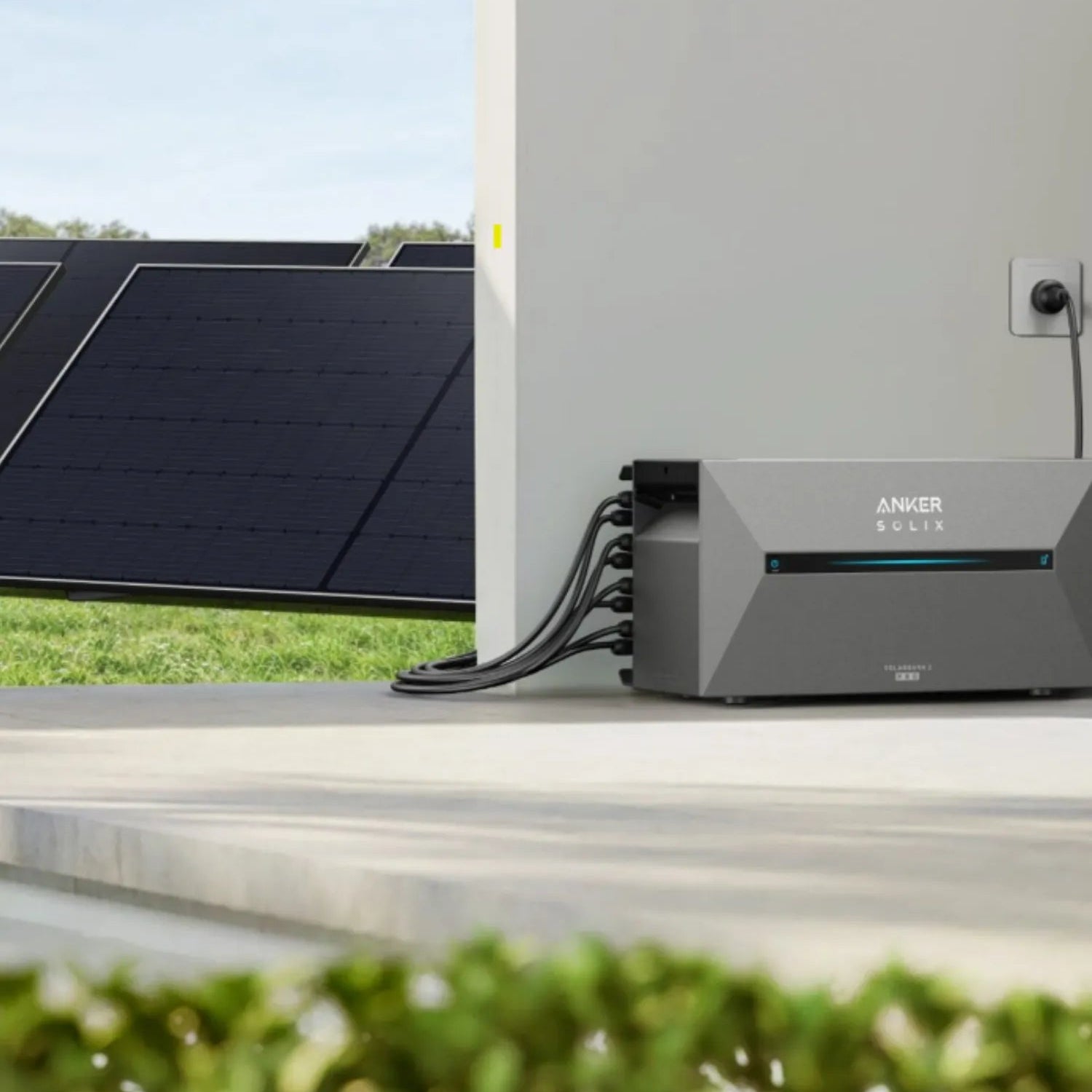 Anker Solix Stromspeicher auf Terasse, an Steckdose angesteckt und mit mehreren Solarmodulen im Hintergrund