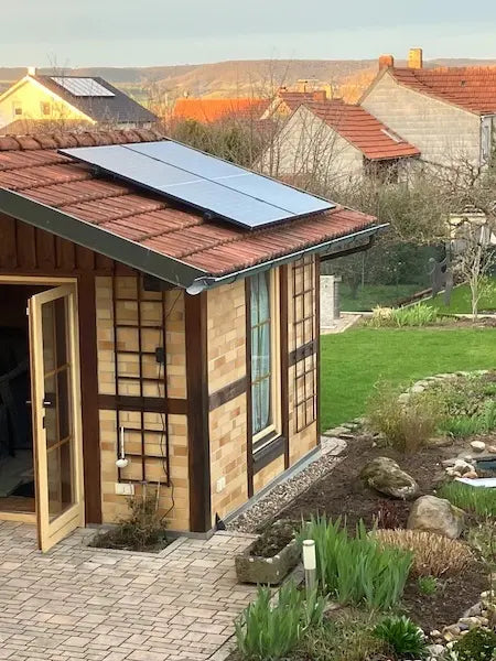 Balkonstrom Basic Roof 860 Watt Balkonkraftwerk mit Trina Solar Solarmodulen auf einem roten Ziegeldach mit Wiese im Hintergrund