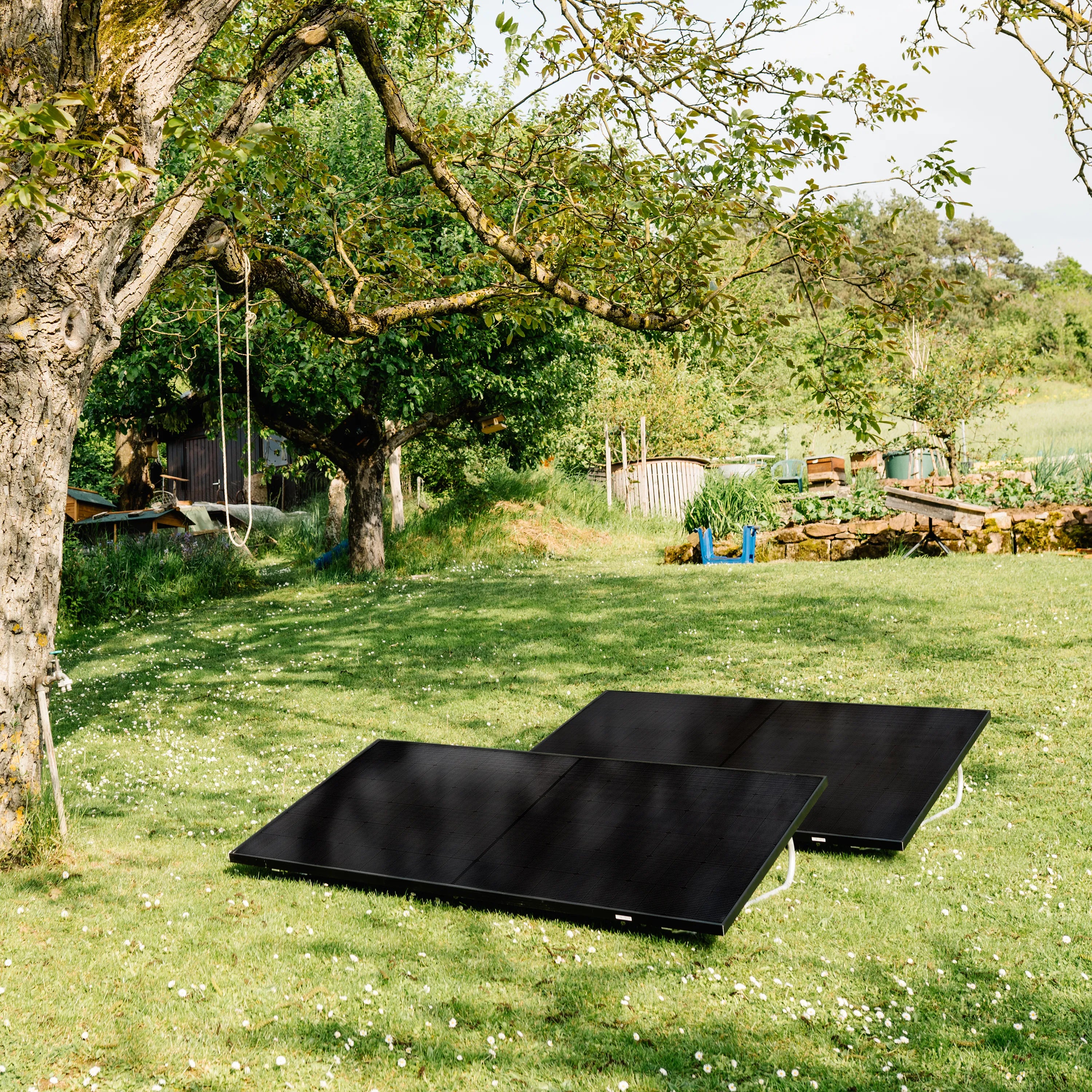 2 schwarze Solarmodule, die in einem Garten auf einer grünen Wiese aufgestellt sind